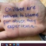 A hand with writing "Children are never to blame for the abuse they experience"